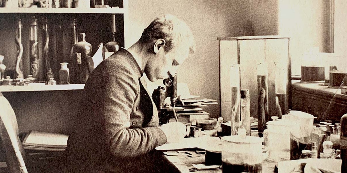 Fridtjof Nansen sitter ved mikroskopet, omgitt av glasskolber med slimål i formalin