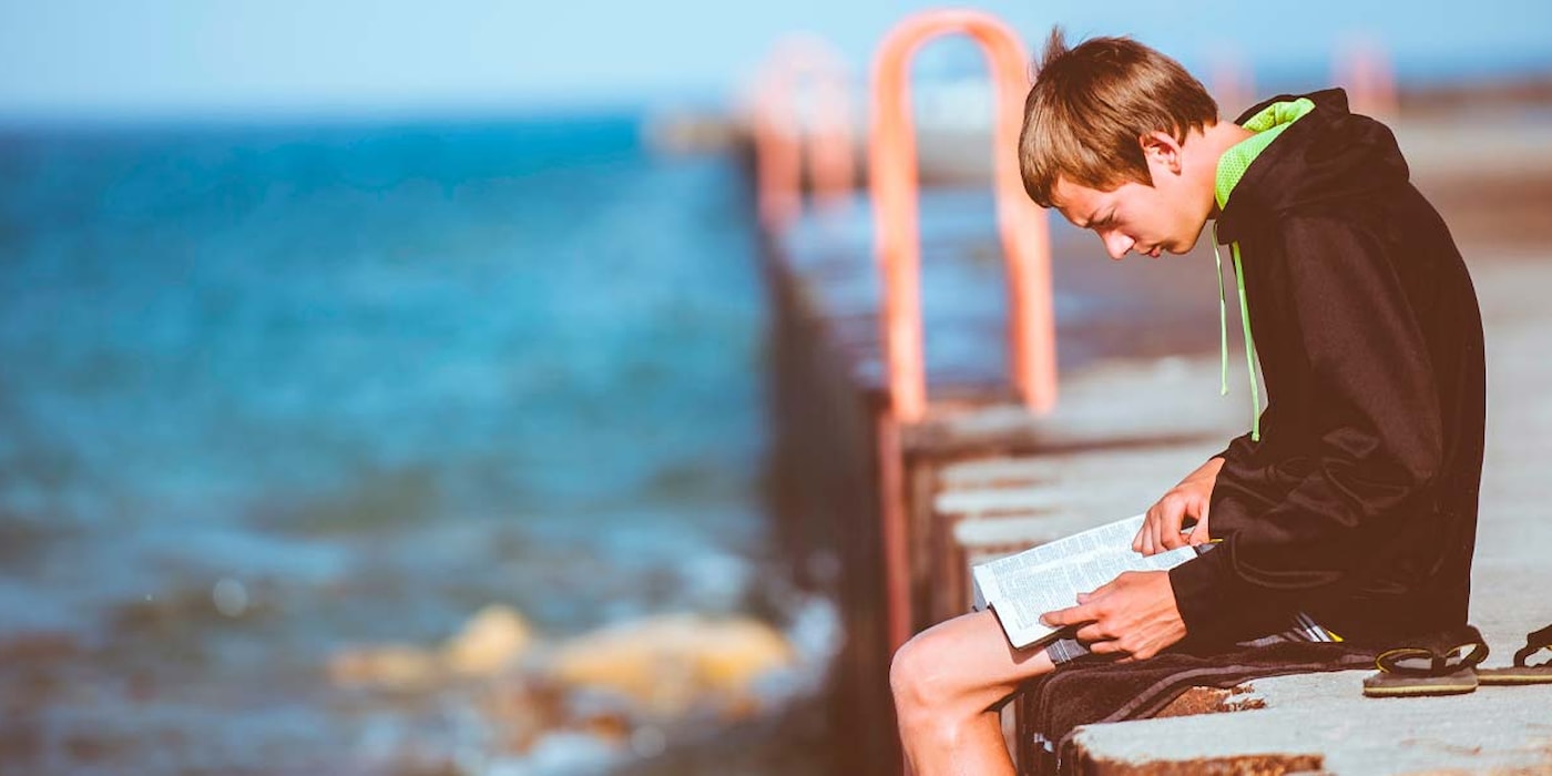 Gutt leser bok på kaien