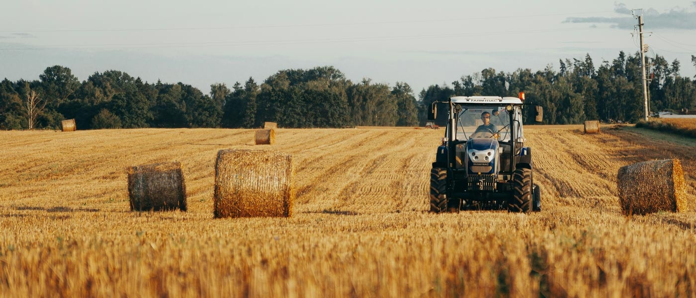 Mann som kjører traktor på jorde med høyballer
