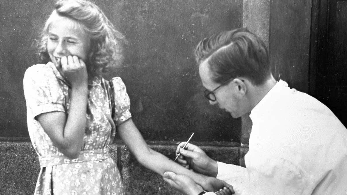 Photo of a schoolgirl of about nine years old and a male physician. She is having a tuberculin test taken on her arm, and it is obvious that it hurts.